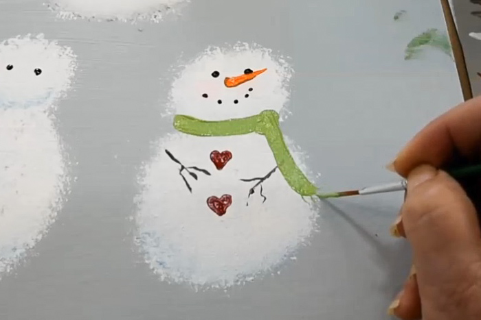 painting a green scarf on snowman with a liner brush