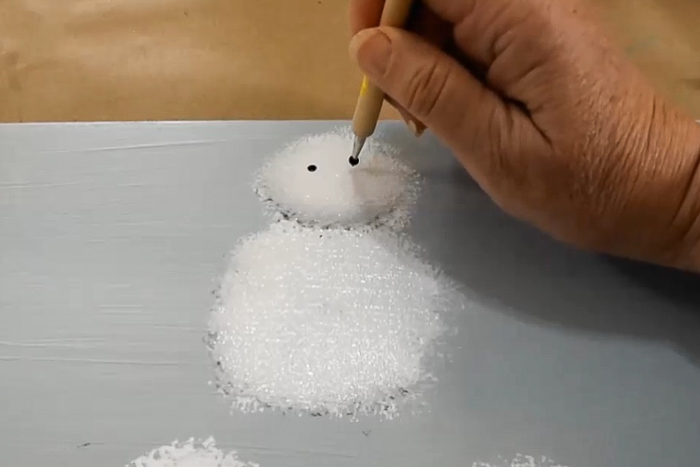 hand placing black dots on painted white circle with stylus to mimic eyes on a snowman