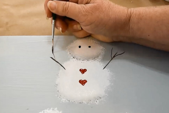 hand with paint brush painting branches for arms on snowman