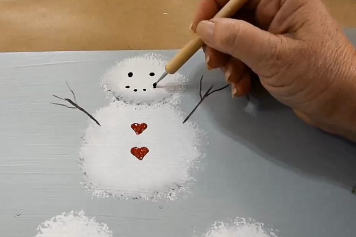 hand dotting a smile onto a snowman with black acrylic paint and a stylus