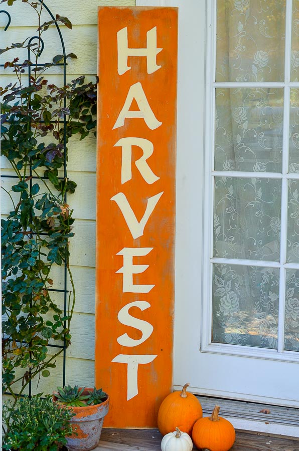 DIY harvest sign setting on the porch with pumpkins and fall plants