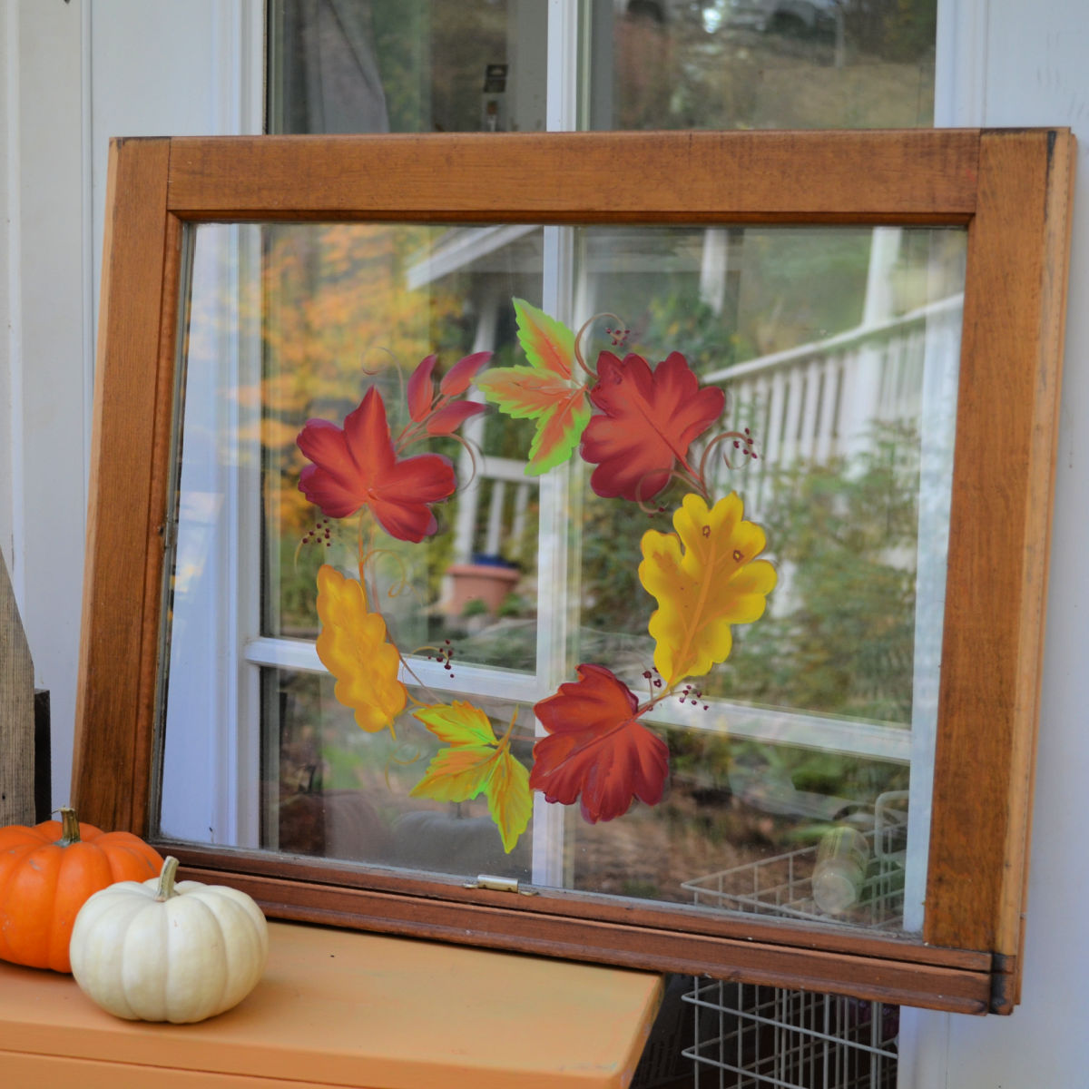 autumn leaves painted on a vintage window setting on an orange bench with mini pumpkins