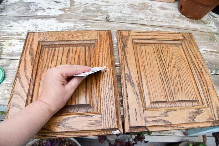 hand scraping wood filler into holes on cabinet doors with a credit card