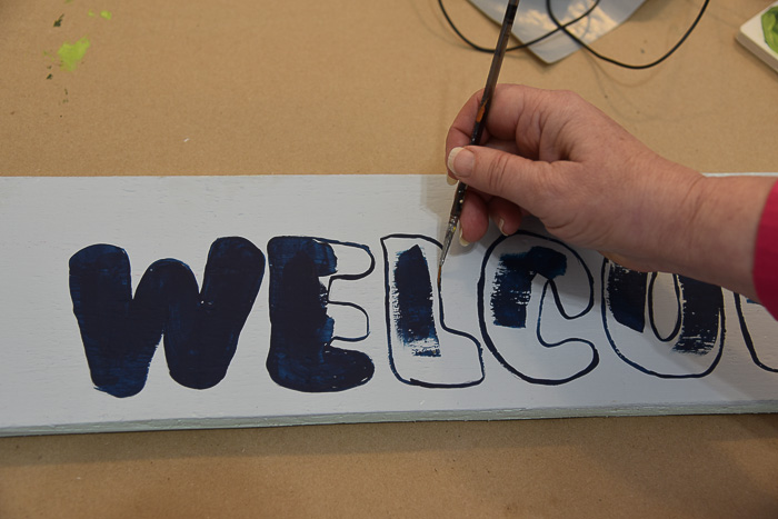 womans had holding a liner paint brush and outlining an L in dark blue paint