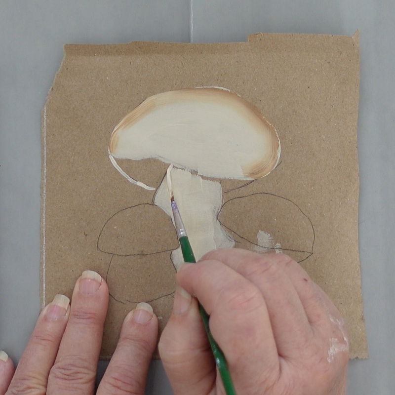 painter using a liner brush to outline the mushroom pattern on a brown paper surface